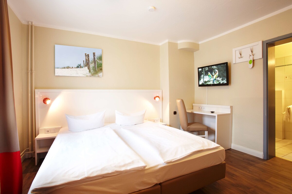 A hotel room with a large bed, a desk, a television, and a painting on the wall.