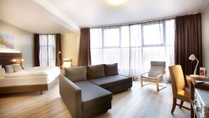 Een hotelkamer met een bed, een bank, een stoel, een bureau en een groot raam met gordijnen.