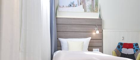A bedroom with a bed, a window with a view, a radiator, and a chair with a colorful cushion.