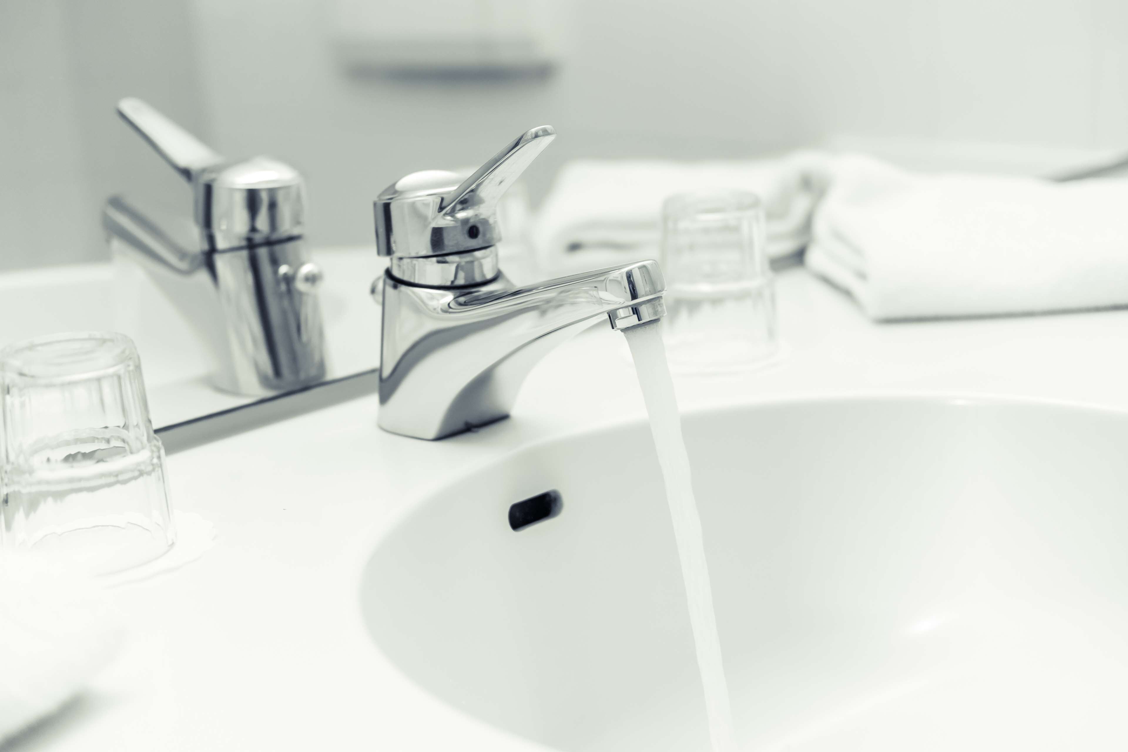A modern bathroom sink with a chrome faucet and clear glass soap dispenser.