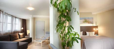 A modern hotel room with a sofa, a chair, a bed, and a large potted plant.