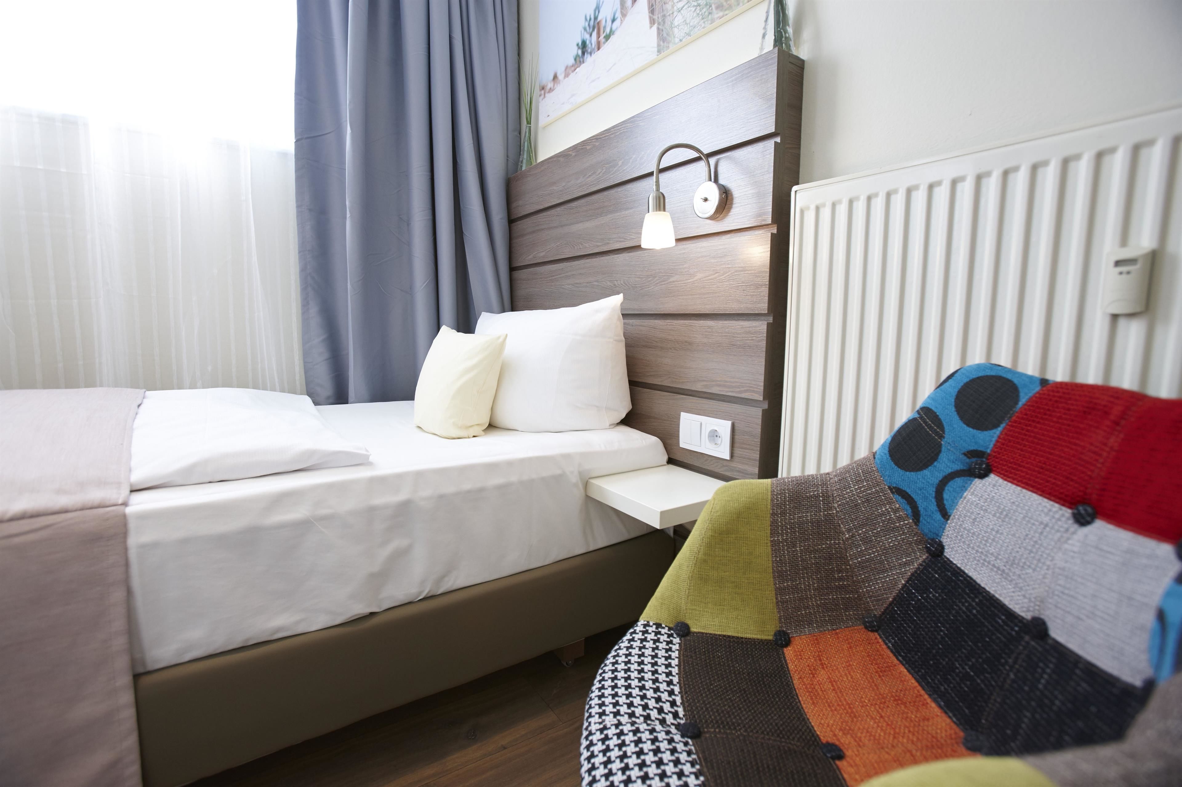 A neatly made bed with white linens, a wooden headboard, and a bedside table with a lamp.