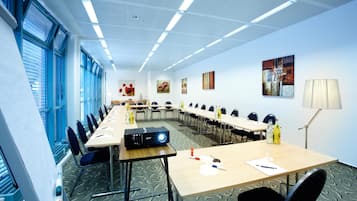 Una sala conferenze con lunghe tavolate, sedie, un proiettore e opere d'arte alle pareti.