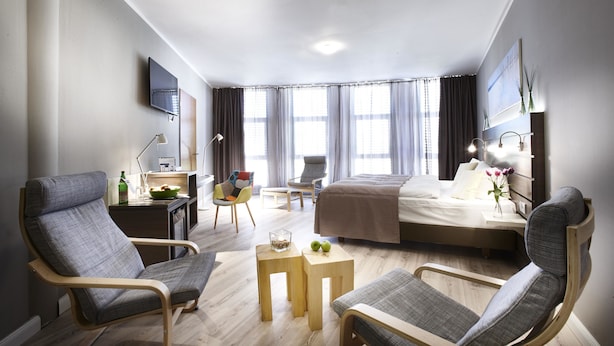 Een moderne hotelkamer met een bed, twee fauteuils, een bureau, een stoel, een klein tafeltje en een televisie.
