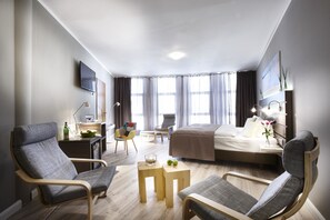 A modern hotel room with a bed, two armchairs, a desk, a chair, a small table, and a TV. - Hotel Kiel by Golden Tulip (Kiel)