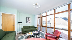 A modern living room with a green sofa, a red chair, a coffee table with a book and a glass of juice, and large windows offering a view of the city. - Staycity Aparthotels, Dublin, Saint Augustine Street (Dublin)