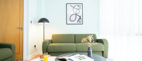 A modern living room with a green sofa, a round coffee table, and a framed abstract artwork on the wall.