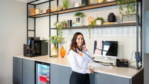 A reception desk with a coffee machine, a computer, and a phone. There are shelves with plants and decorative items. - Staycity Aparthotels, Dublin, Saint Augustine Street (Dublin)