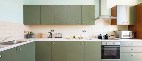 A kitchen with green cabinets, a microwave, a toaster, and a kettle.