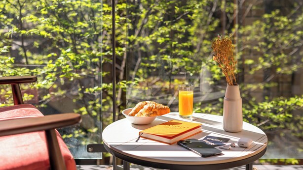 A breakfast table with croissants, a glass of orange juice, a book, a vase with dried flowers, and a smartphone on a balcony overlooking a forest. - Staycity Aparthotels, Dublin, Saint Augustine Street (Dublin)