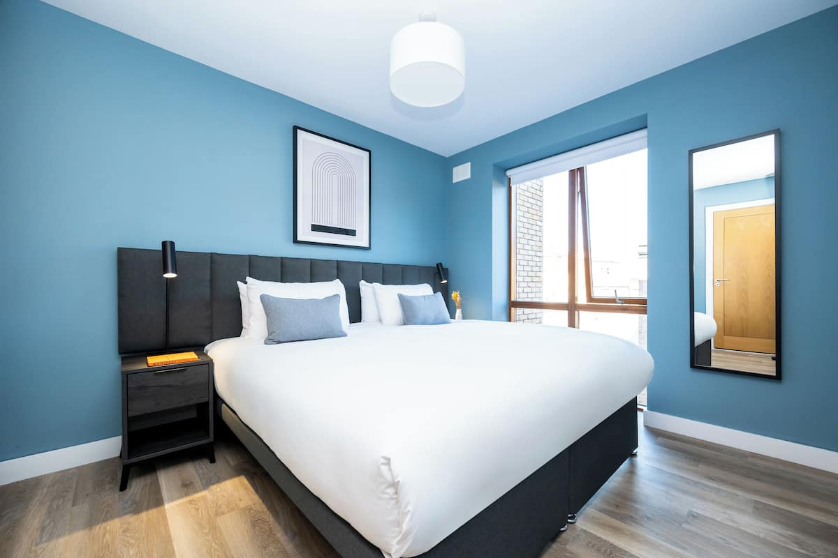 Een moderne slaapkamer met een groot bed, een nachtkastje, een ingelijst schilderij en een raam met uitzicht.