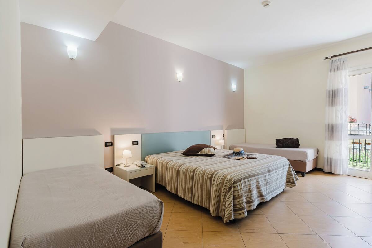 A hotel room with two beds, a desk, a chair, and a window with curtains.
