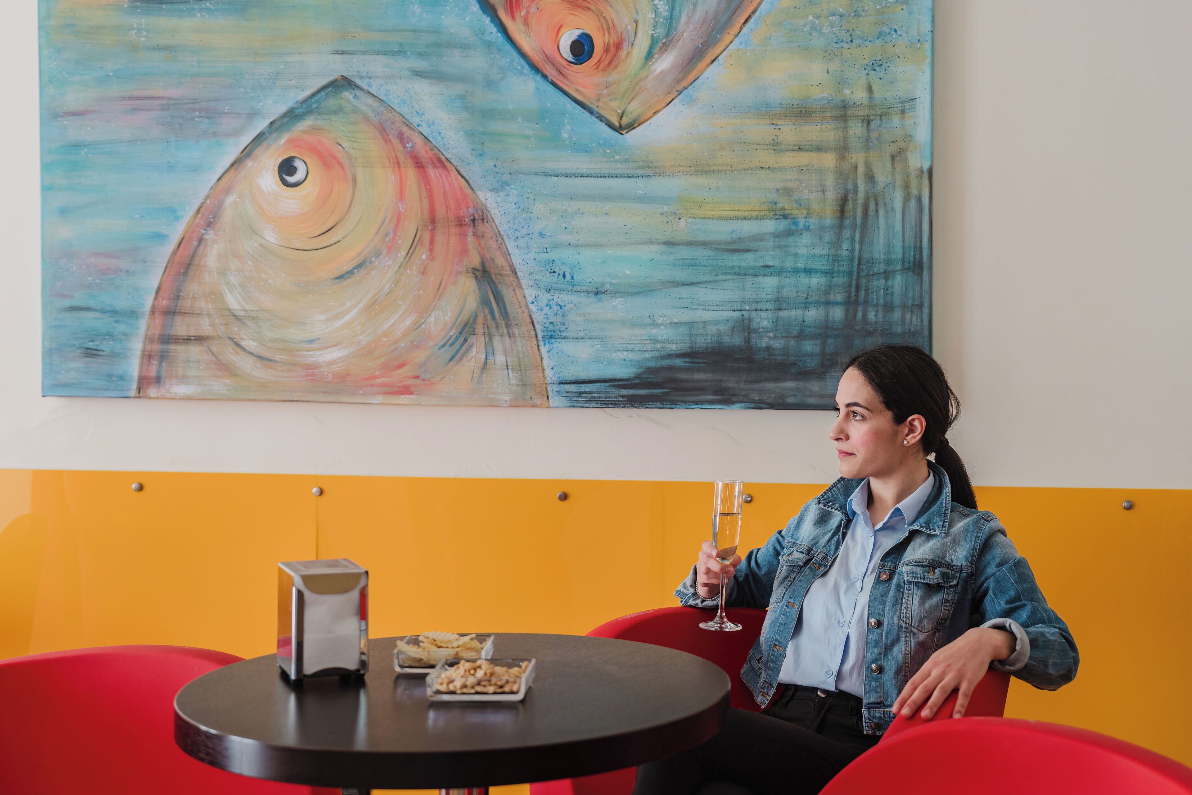 Una persona sentada a una mesa redonda con una bebida en un vaso, un plato de comida y una cafetera.
