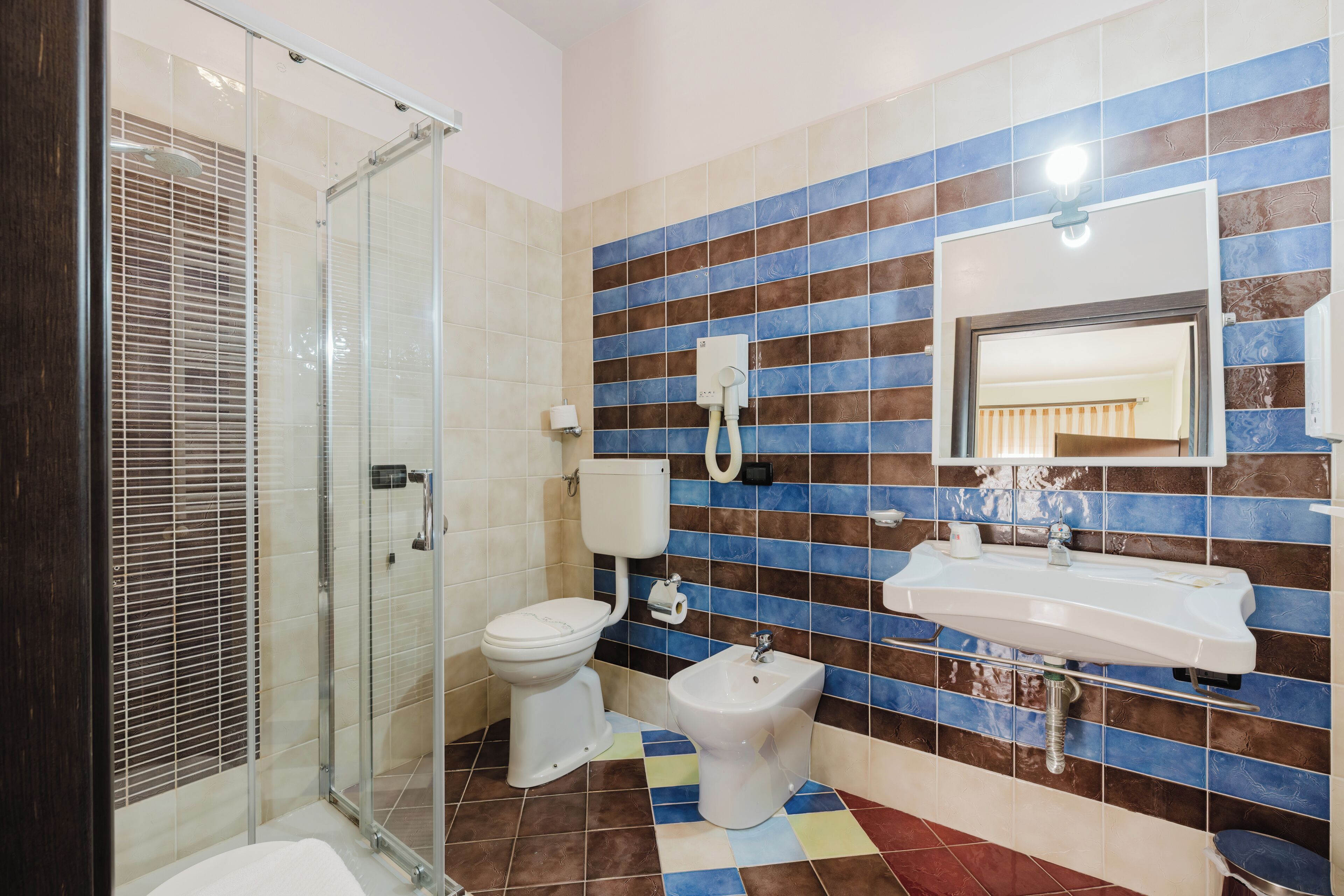 A bathroom with a glass shower enclosure, a toilet, a bidet, and a sink with a mirror.