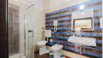 A bathroom with a glass shower enclosure, a toilet, a bidet, and a sink with a mirror.