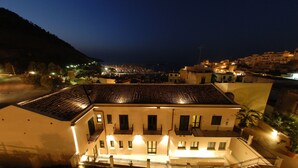 Un edificio de varios pisos con balcones, un patio interior y vistas de un pueblo por la noche.