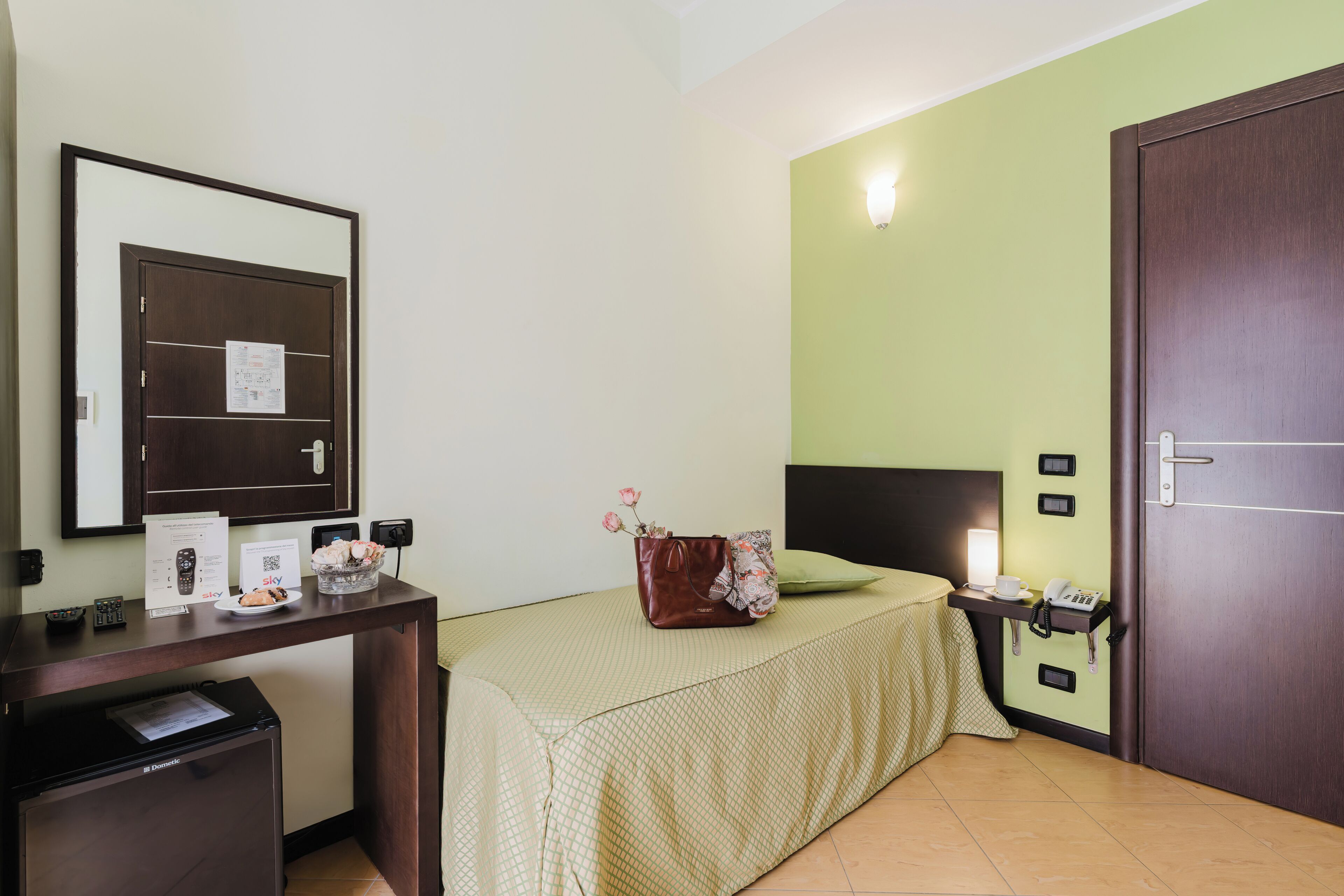 A hotel room with a bed, bedside table, desk, and a wardrobe.