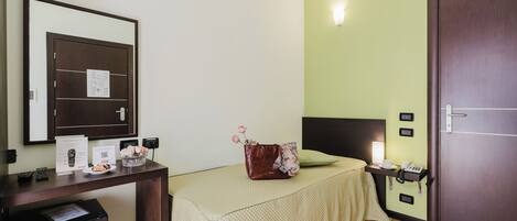 A hotel room with a bed, bedside table, desk, and a wardrobe.