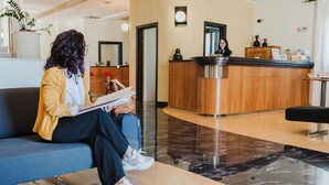 Zona de recepción con mostrador de madera, una recepcionista, un sofá azul y una mesa de recepción.