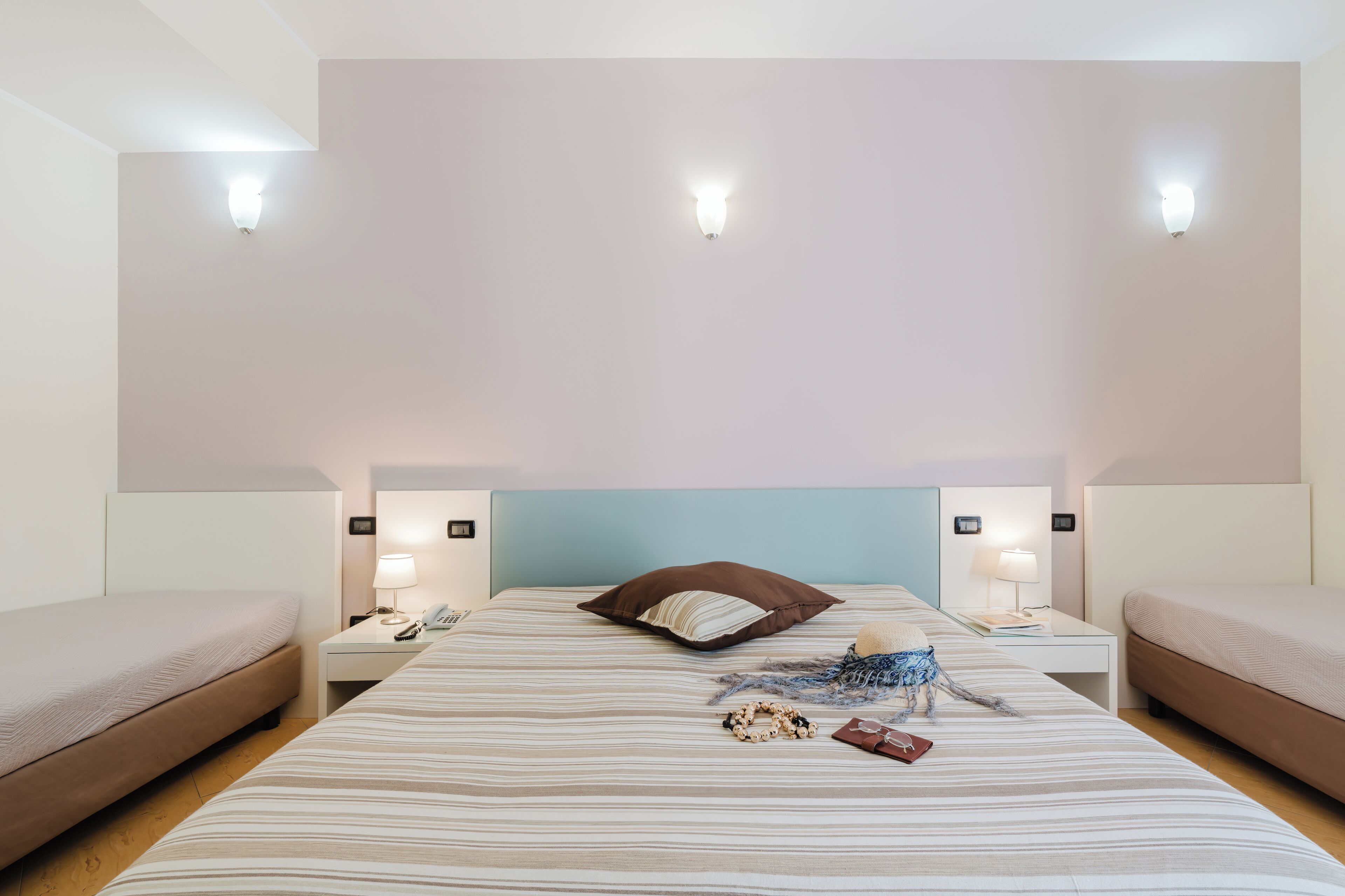 A hotel room with a large bed, two bedside tables, a nightstand, a headboard, and wall-mounted lighting.