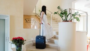 Una mujer bajando una escalera con una maleta, una planta en maceta y un letrero con un logotipo.
