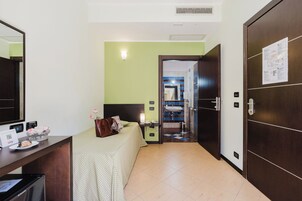 Habitación de hotel con cama, mesita de noche y escritorio con computadora. Se ve un baño a través de una puerta abierta.