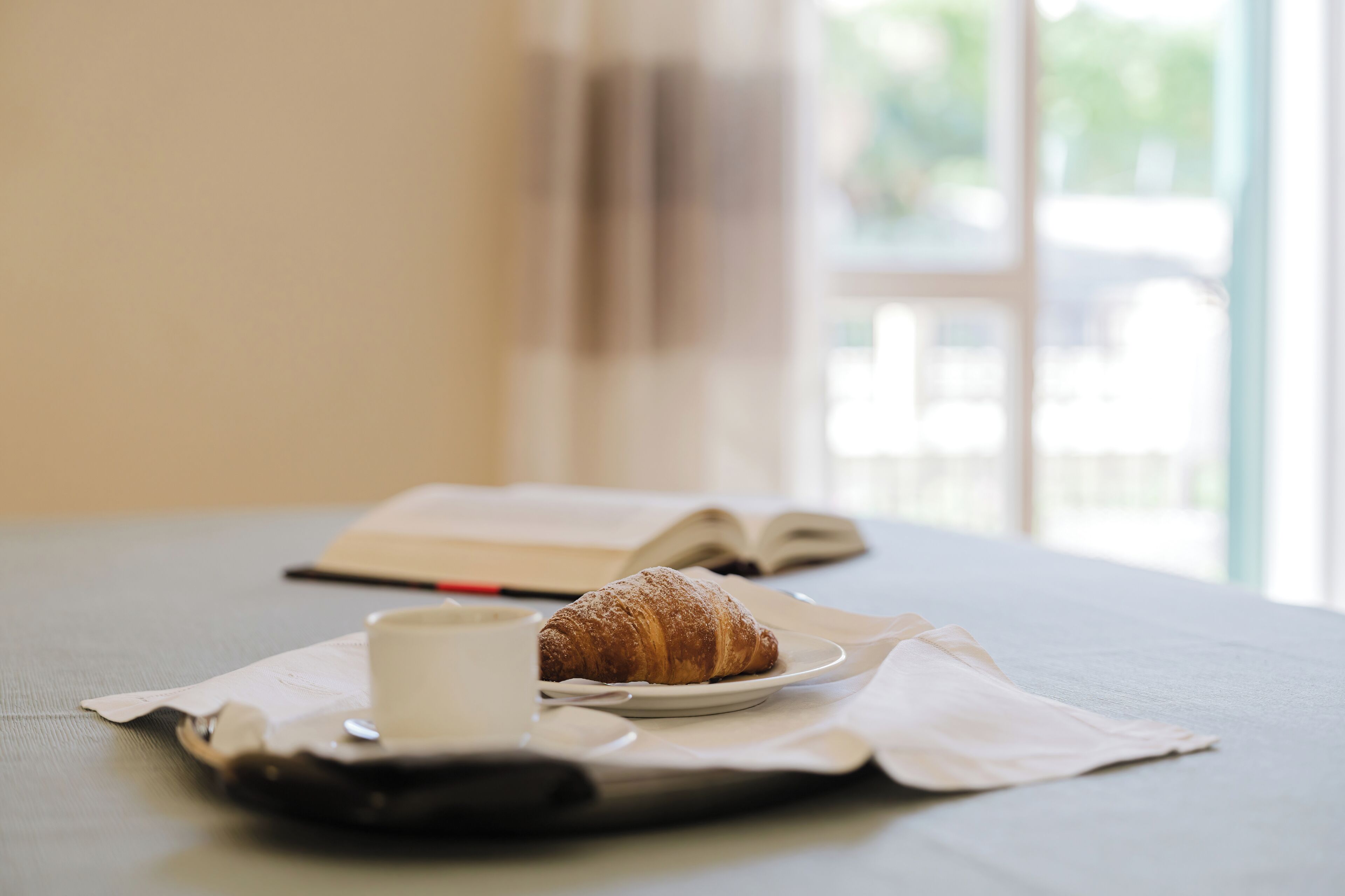 A table with a croissant, a cup, and an open book.