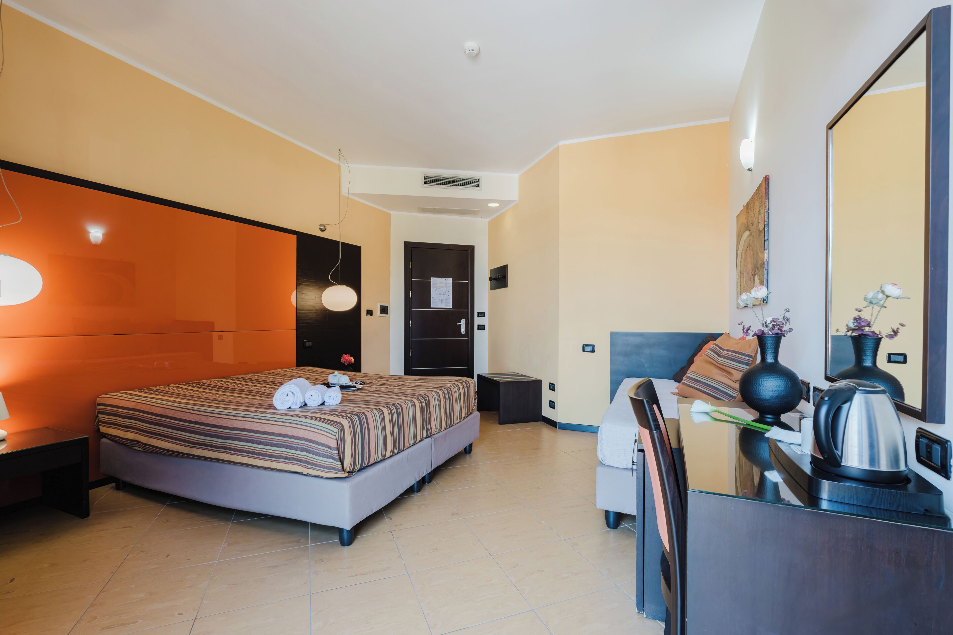 Une chambre d’hôtel moderne avec un grand lit, un bureau doté d’une bouilloire et un miroir.