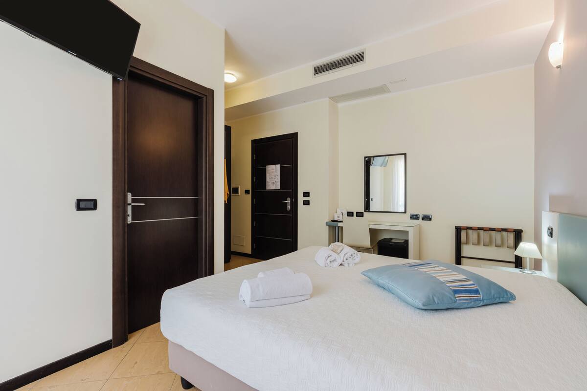 A hotel room with a bed, a desk, a mirror, and a door.