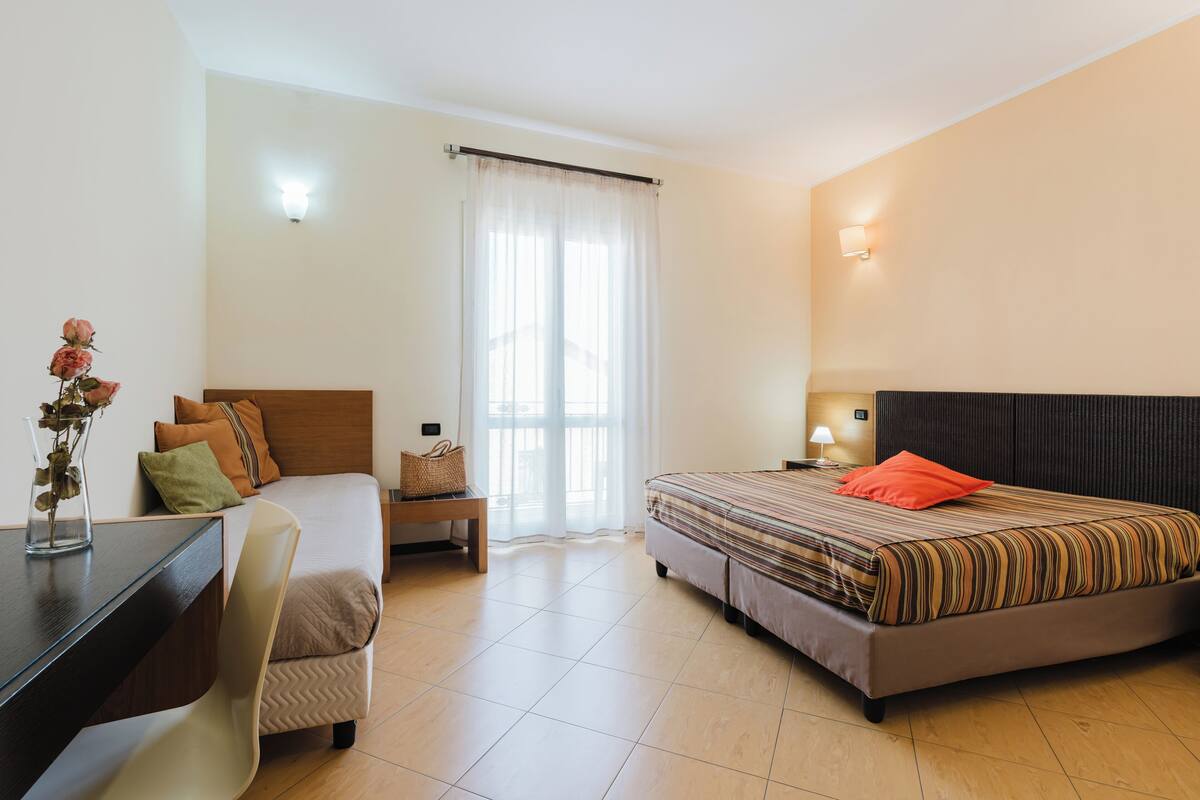 A bedroom with a bed, bedside table, lamp, chair, and a desk with a vase.