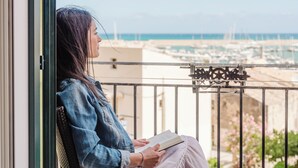 Una persona leyendo un libro en un balcón con vista a un puerto deportivo y barcos.