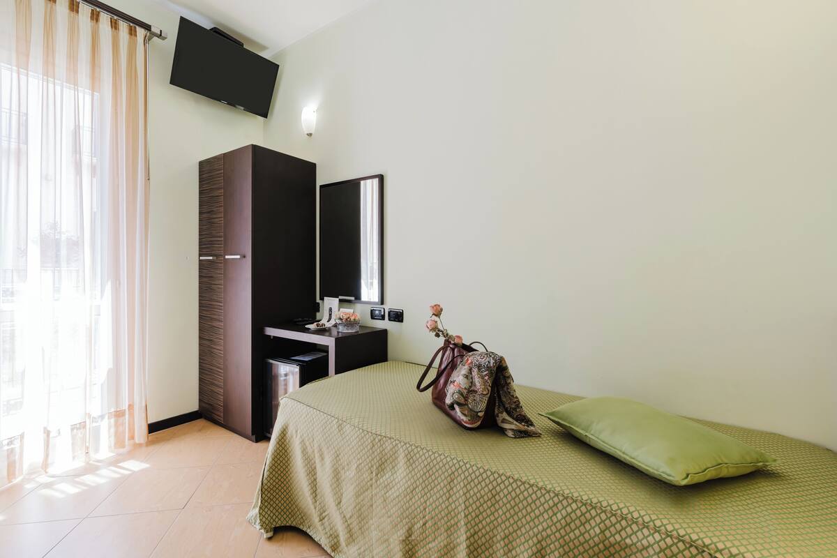 A bedroom with a bed, a dresser, a TV, and a window with curtains.