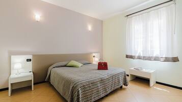 Quarto com cama, mesas de cabeceira, luminária na parede e cortinas na janela.