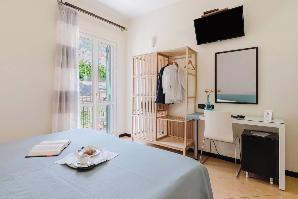 A hotel room with a bed, a desk, a wardrobe, and a TV on the wall.