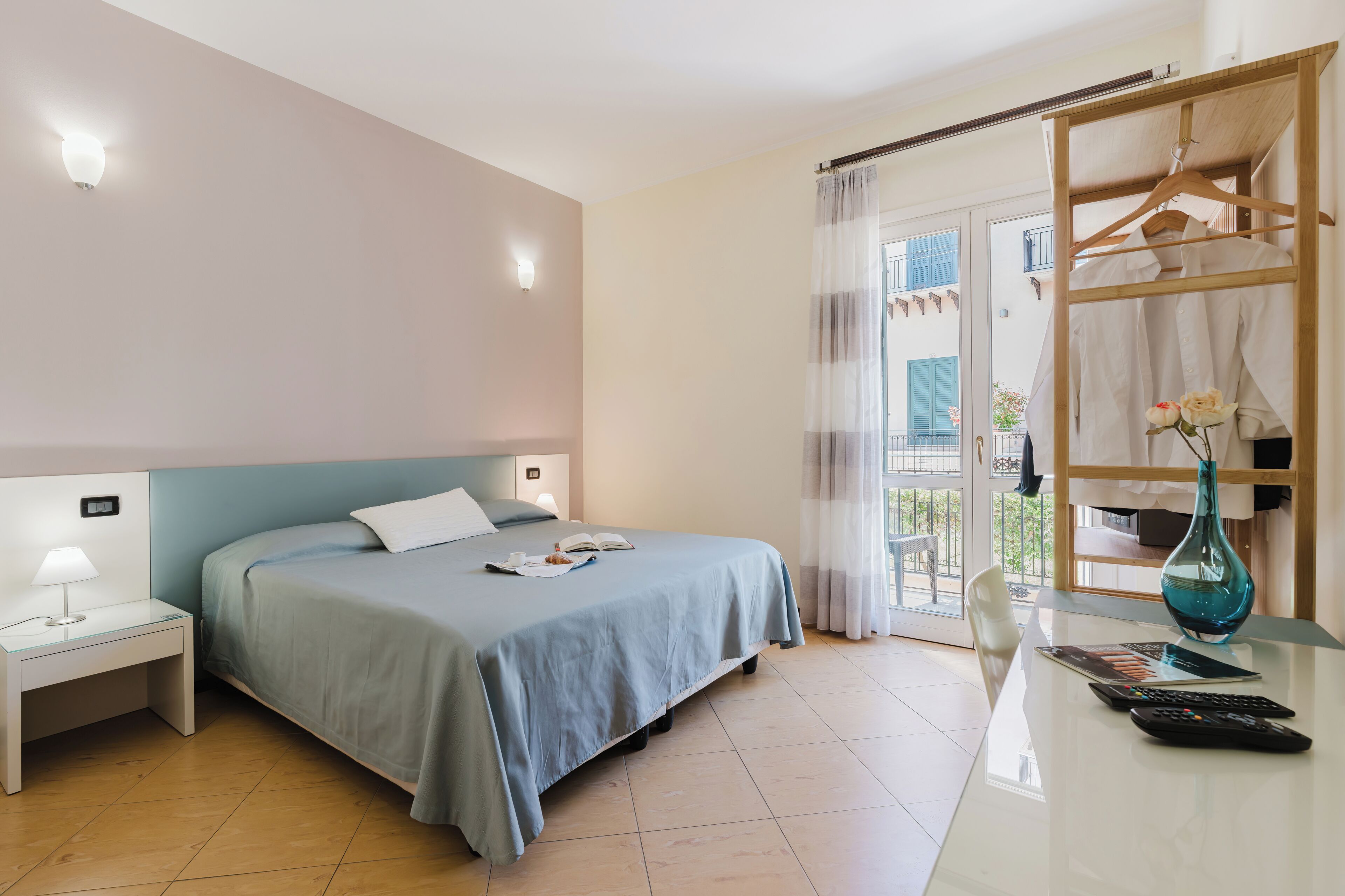 A bedroom with a bed, bedside table, lamp, and a view of the outside.