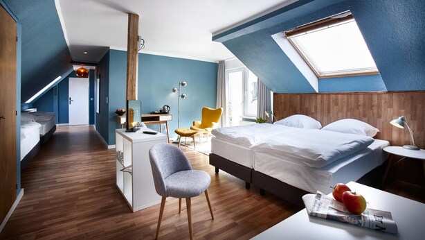 Un dormitorio moderno con techo inclinado, cama, escritorio, silla y ventana.