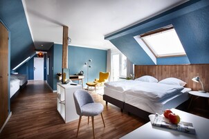 A modern bedroom with a sloped ceiling, a bed, a desk, a chair, and a window.