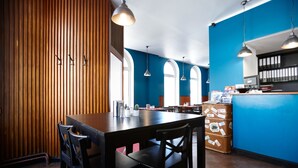 Un restaurante con pared de madera, paredes azules y ventanas arqueadas. Hay mesas y sillas, además de un mostrador con una caja registradora.