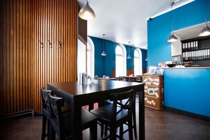A restaurant with a wooden wall, blue walls, and arched windows. There are tables and chairs, and a counter with a cash register.