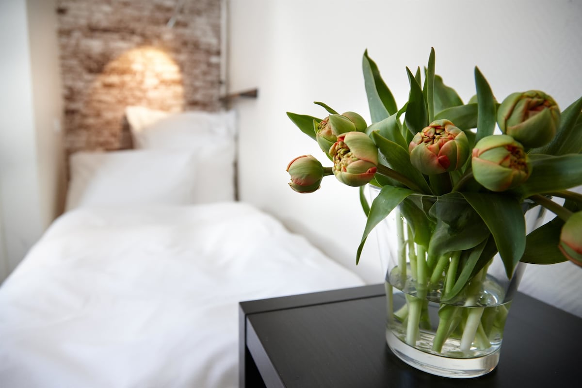 A bed with white linens and a nightstand with a vase of tulips.