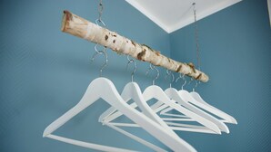 Una rama de madera con perchas blancas sobre un muro azul.