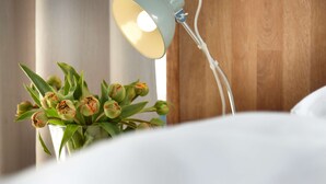 Una cama con ropa de cama blanca, una lámpara de noche y un jarrón con tulipanes verdes.