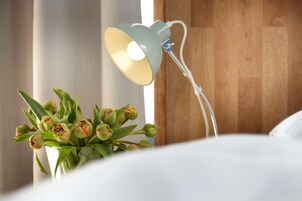 A bed with white bedding, a bedside lamp, and a vase with green tulips.