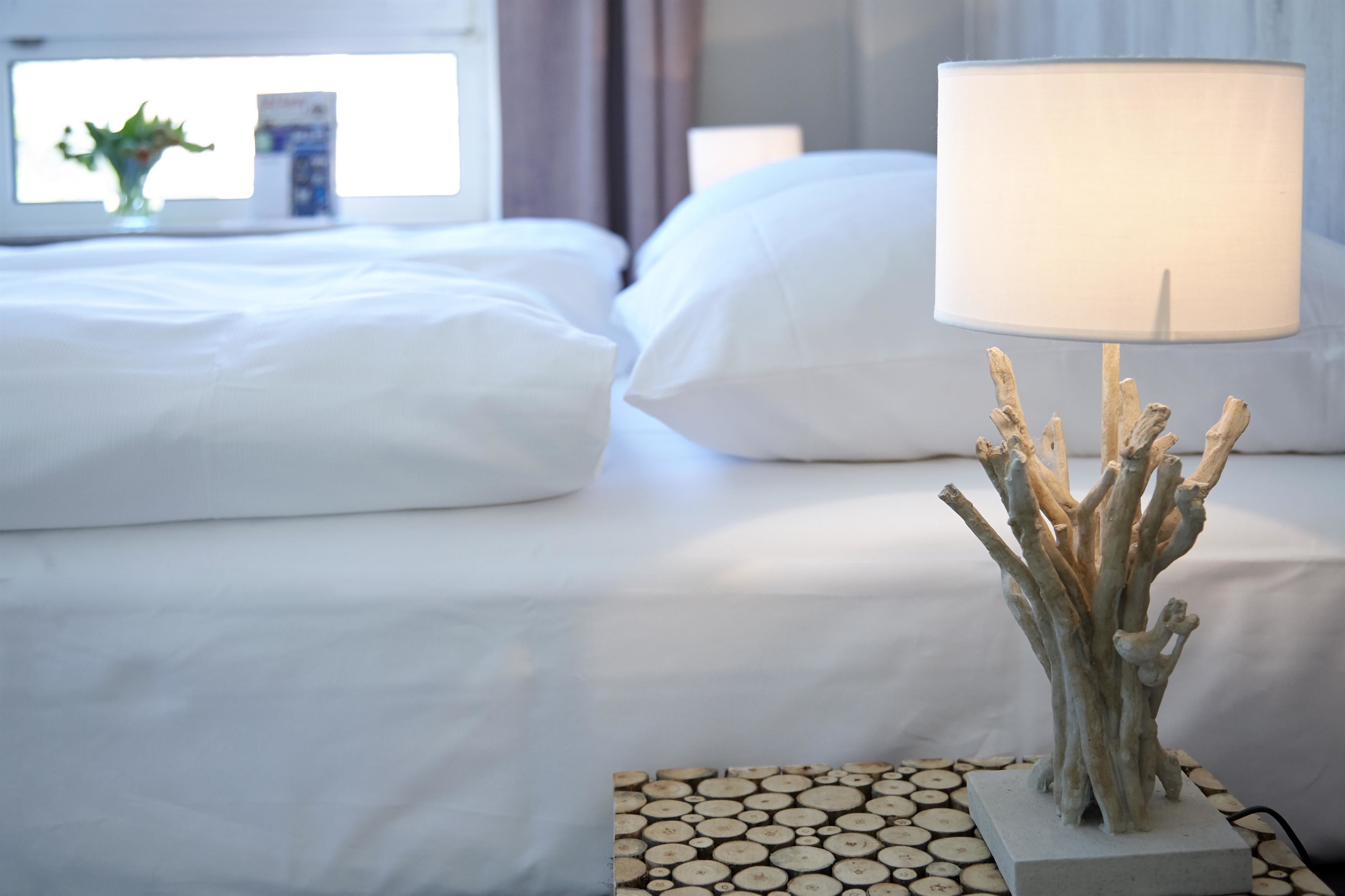 A neatly made bed with white linens, a bedside lamp with a white shade, and a decorative wooden sculpture on a bedside table.