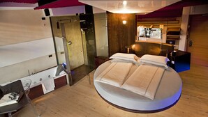 A modern bedroom with a circular bed, a glass shower enclosure, and a wooden floor. - Ambienthotel Primaluna (Malcesine)