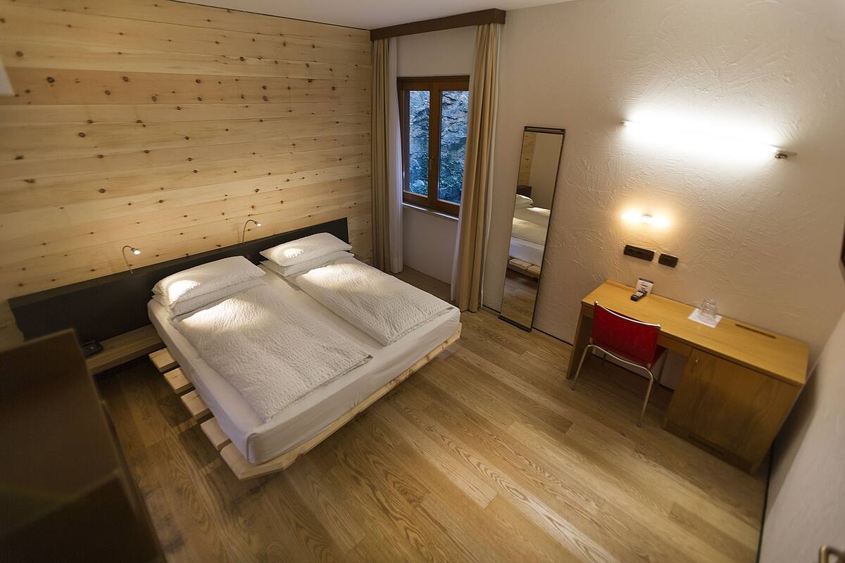 A bedroom with a wooden headboard, a bed with white linens, a desk with a chair, and a mirror on the wall.