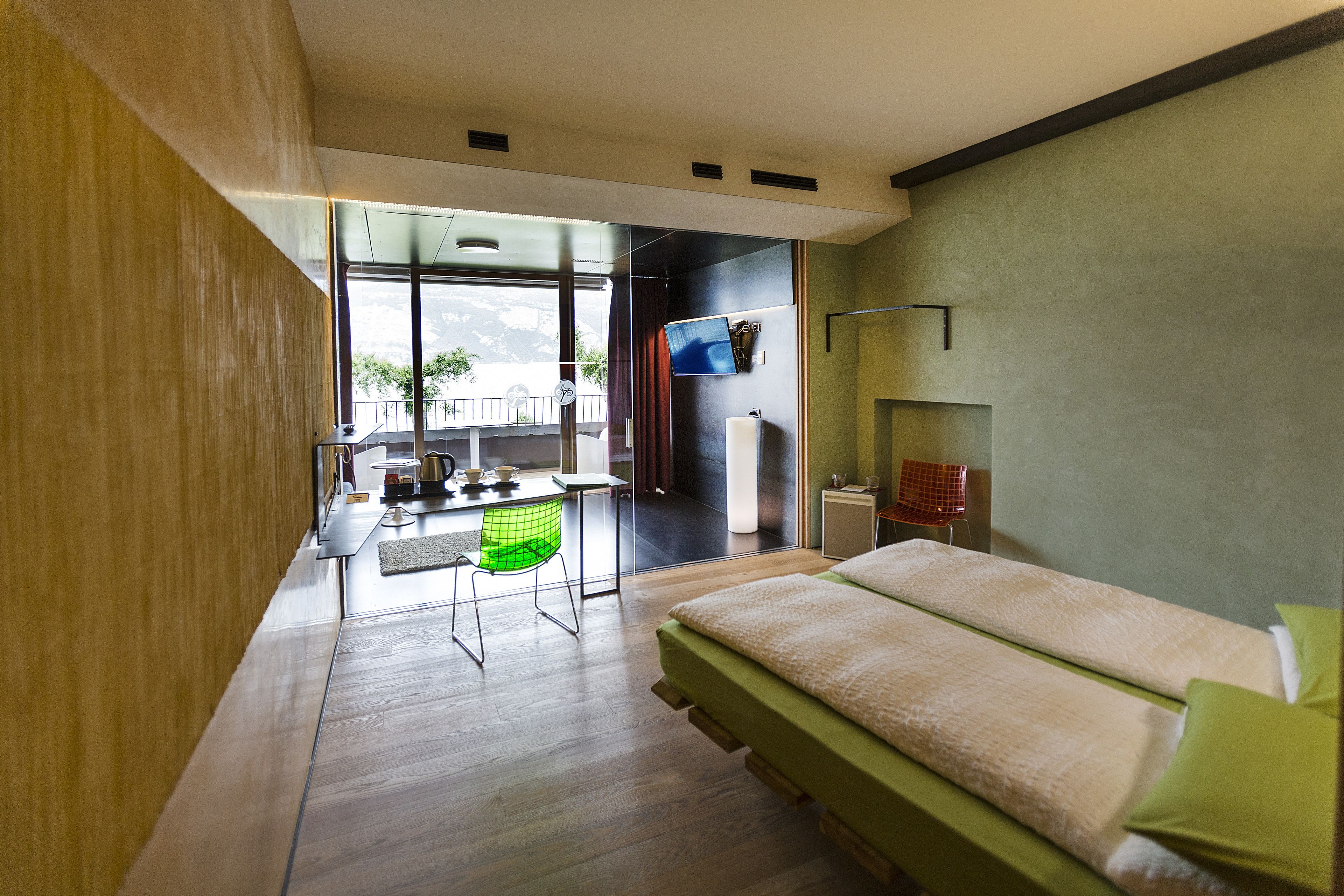 A modern hotel room with a large bed, a desk, and a view of the outdoors.