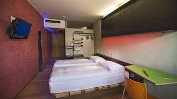 Habitación de hotel con dos camas, un escritorio, un televisor y un baño visible a través de una puerta abierta.