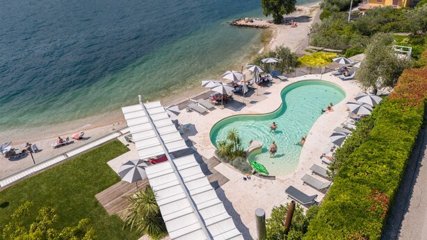A resort with a swimming pool, sun loungers, and a beach area. - Ambienthotel Primaluna (Malcesine)