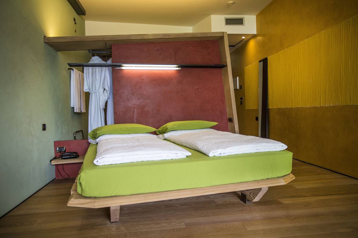 A bed with green bedding, a wooden headboard, and a red accent wall.